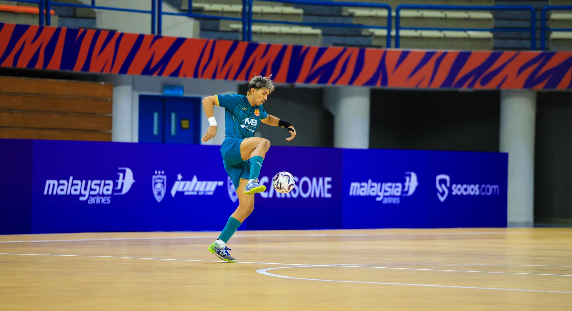 MPFL player controlling the ball mid-air on a futsal court, with Malaysia Airlines, Johor Darul Ta'zim, Carsome and Socios.com sponsor boards behind